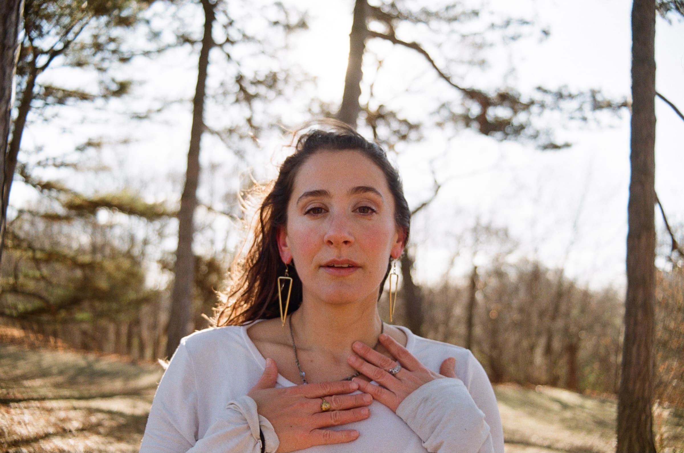 Avery standing among pine trees, hands resting on her chest