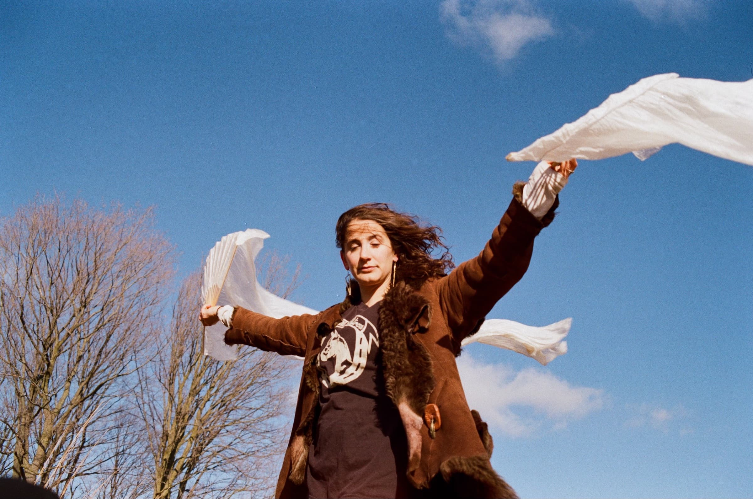 Avery outdoors, arms open, white silk streaming in the wind